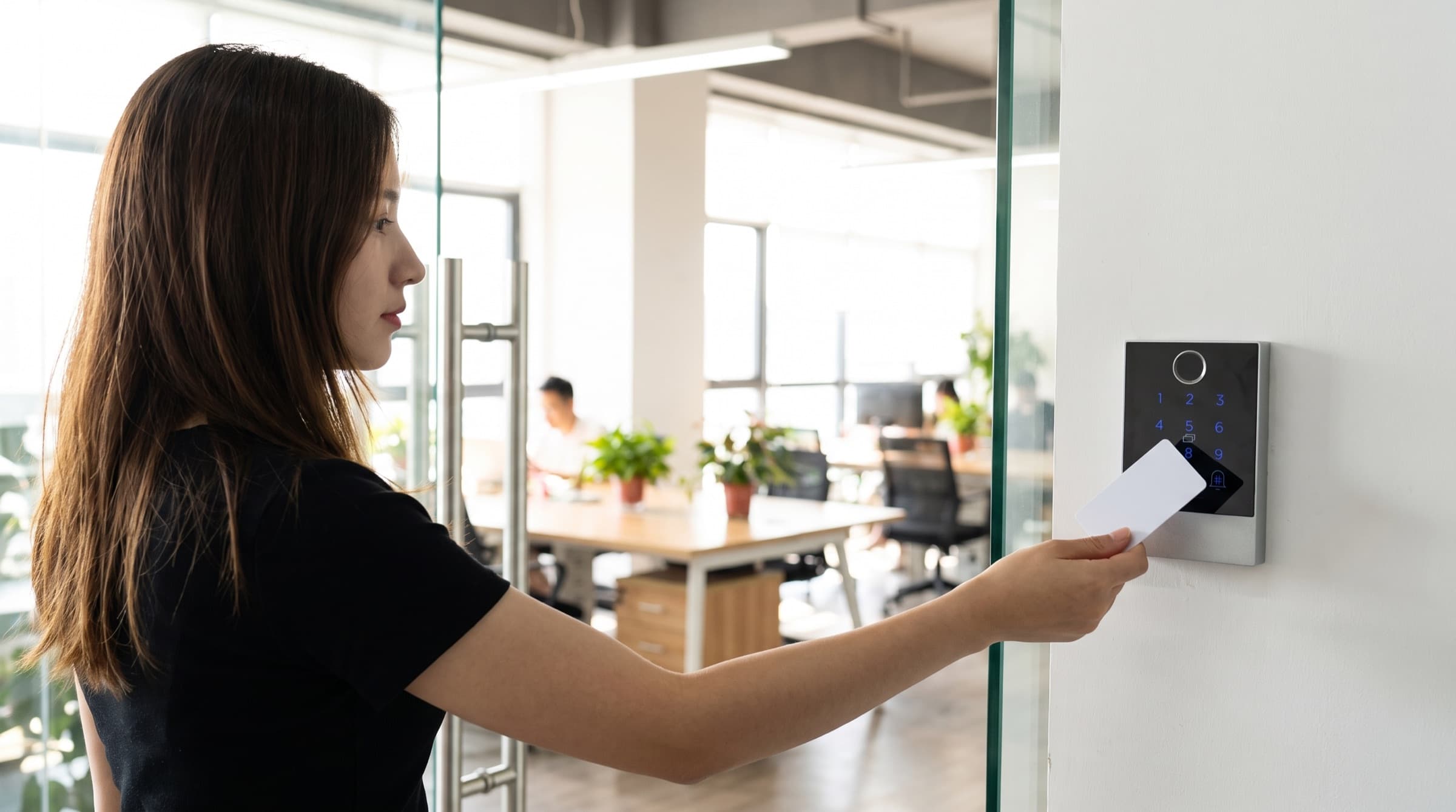 Access card held to the wall-mounted reader beside an office glass door